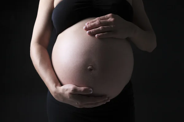 Hamile bir kadının siyah arka plan üzerine bir göbek — Stok fotoğraf