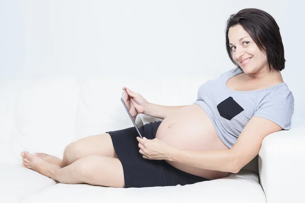 Mulher grávida feliz olhando para a câmera, usando um tablet digital — Fotografia de Stock