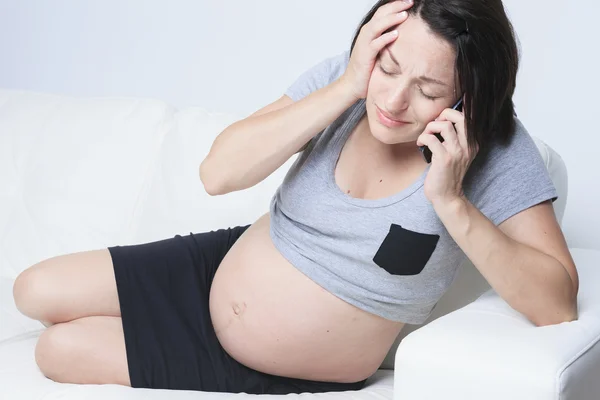 Donna incinta seduta sul divano con un telefono — Foto Stock