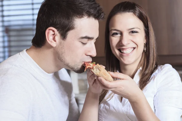 A Happy young couple eating pizza at the kitchen — Stock Photo, Image