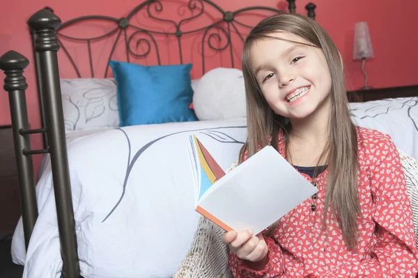 Een mooi klein meisje zitten haar slaapkamer met een boek — Stockfoto