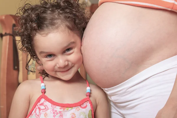 Little cute girl looking at her mother pregnant tummy — Stock Photo, Image