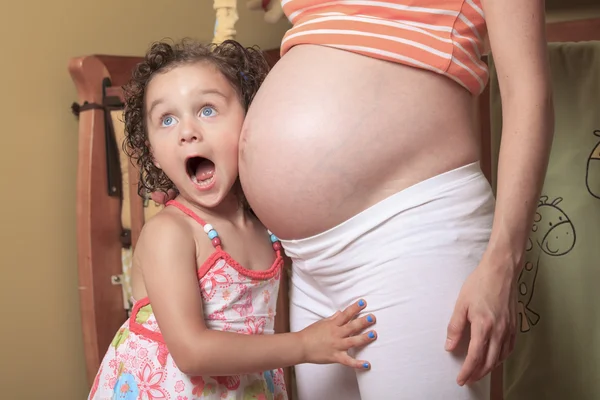 Kleines süßes Mädchen mit Blick auf ihren schwangeren Bauch — Stockfoto