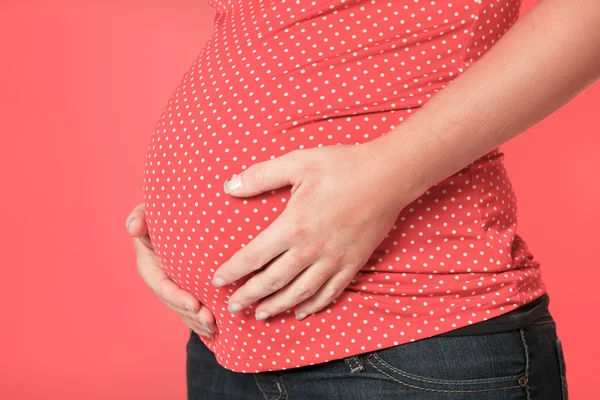 Een mooie zwangere vrouw op rode achtergrond — Stockfoto