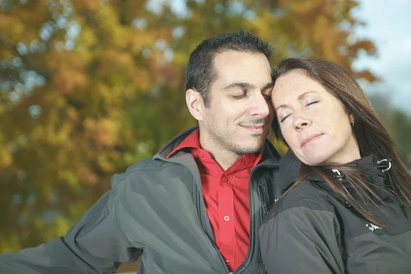 Una pareja amorosa sentada en el banco en el fondo de otoño —  Fotos de Stock