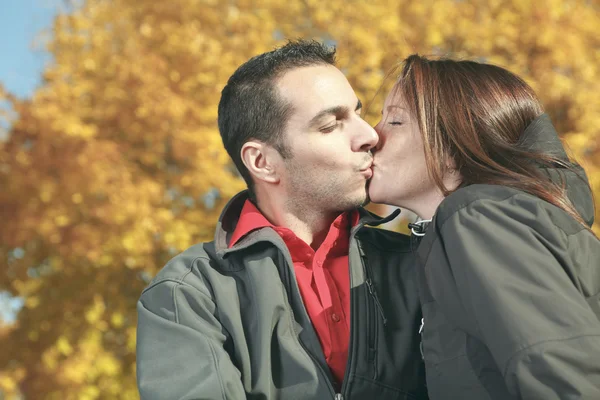 Una pareja amorosa sentada en el banco en el fondo de otoño — Foto de Stock