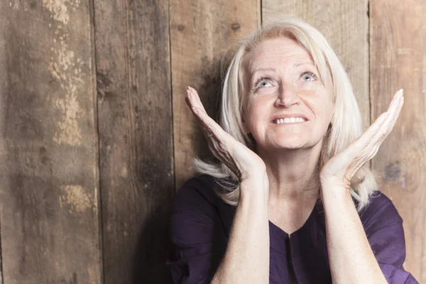 Een senior vrouw bidden met een houten achtergrond — Stockfoto