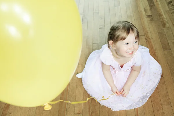 Ein nettes kleines Mädchen sitzt mit einem Luftballon auf dem Boden — Stockfoto