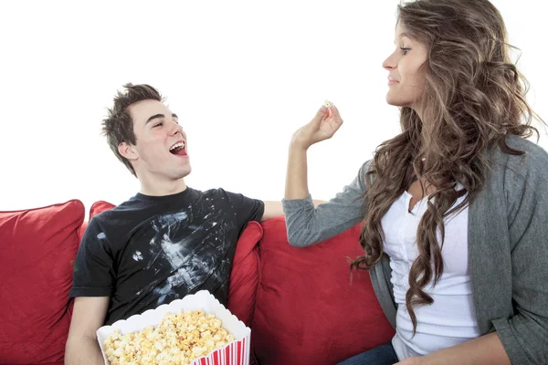 Primer plano retrato de pareja joven sentados juntos en un sofá en casa viendo la televisión, sonriendo alegremente comiendo maíz pop disfrutando de una noche juntos. Hogar estilo de vida y tecnología de entretenimiento . — Foto de Stock