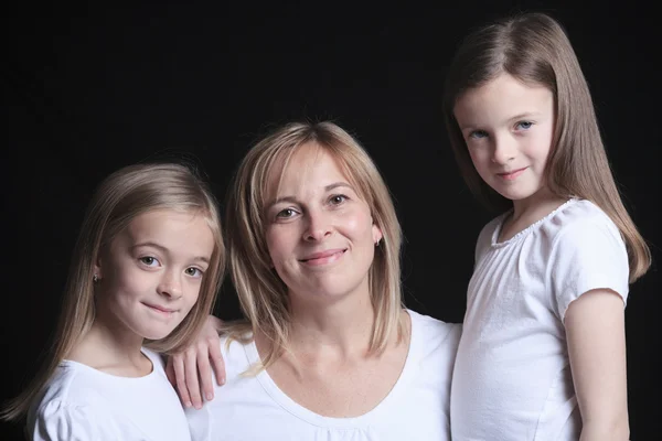 Uma mãe com é duas filhas sobre fundo escuro — Fotografia de Stock
