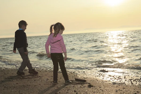 Duas crianças felizes brincando na praia ao pôr do sol — Fotografia de Stock