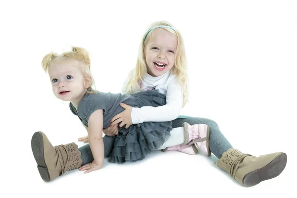 Two cute little blond sisters kneeling on the floor arm in arm c — Stock Photo, Image