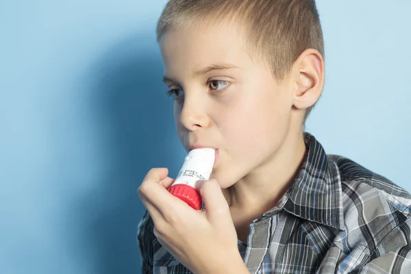 Un niño con asma es inhalador sobre fondo azul —  Fotos de Stock