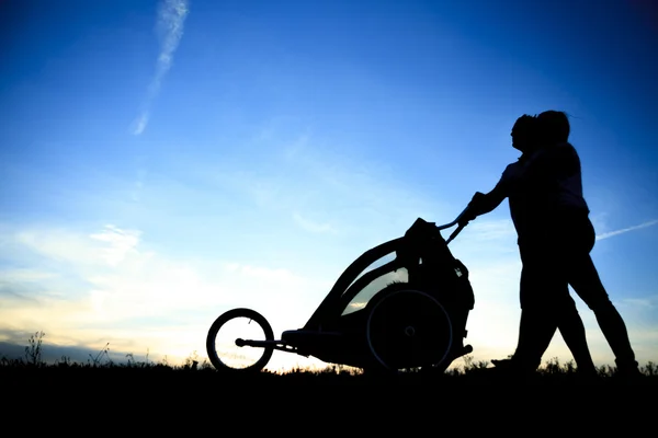Silhouettes of parents loving  their child in a stroller — Stock Photo, Image