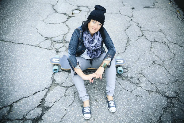 Beautiful young woman sitting over a skateboard — Stock Photo, Image