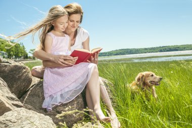 Little girl with mother reading a book in a summer park clipart