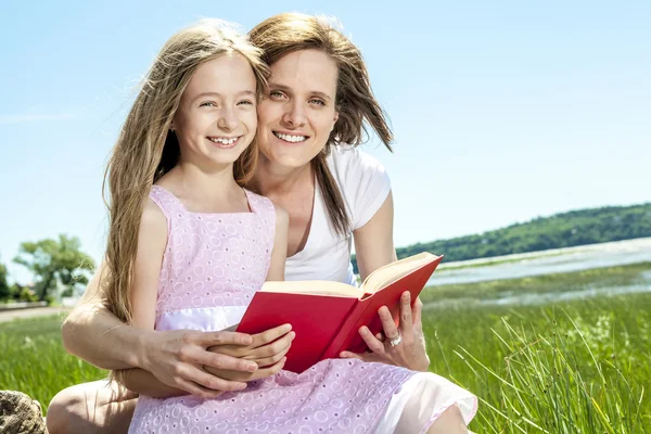 Kleines Mädchen mit Mutter liest im Sommerpark ein Buch — Stockfoto