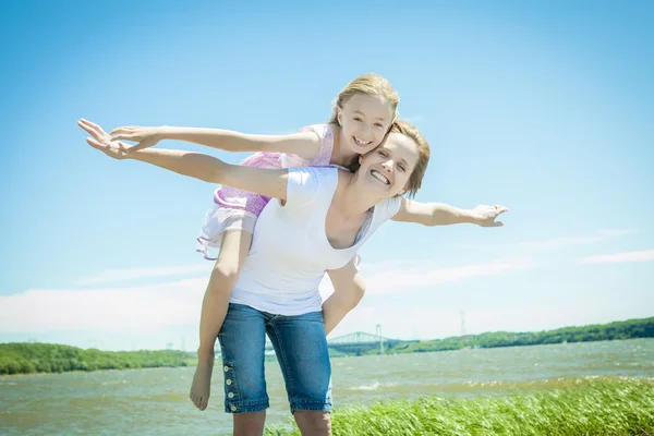 Junges Mädchen umarmt ihre Mutter huckepack Stil — Stockfoto