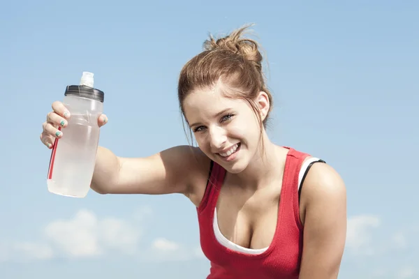 Jonge, sportieve vrouw drinking water uit een fles tegen de blauwe hemel — Stockfoto