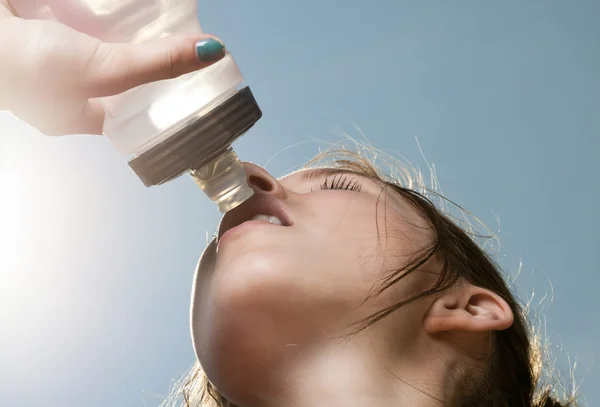 Joven deportista bebiendo agua de una botella contra el cielo azul —  Fotos de Stock