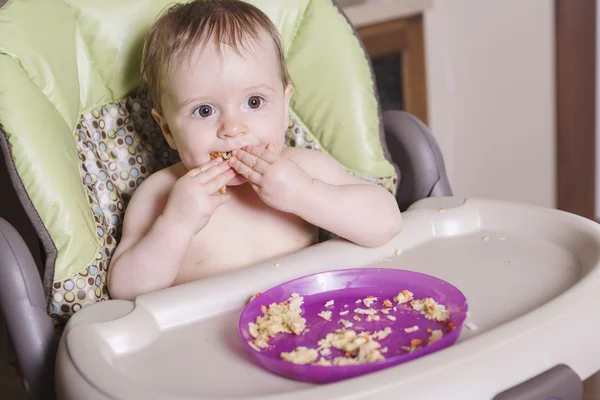 Babysitting in hoge-stoel eten met haar hand — Stockfoto