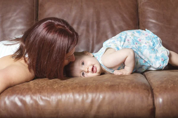 Happy beautiful young mother and baby laying on sofa — Stock Photo, Image