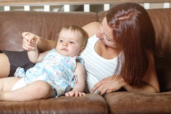 Happy beautiful young mother and baby laying on sofa — Stock Photo, Image