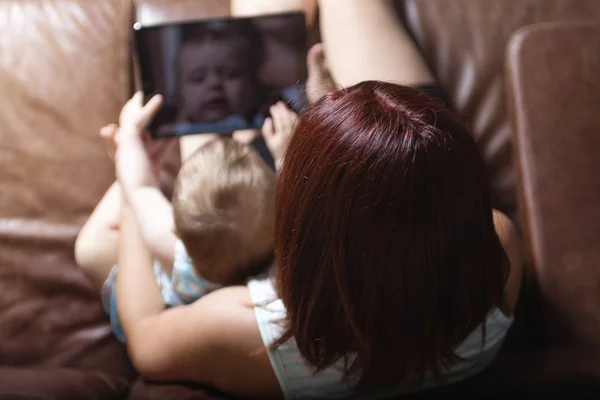 母親と赤ちゃんは自宅のソファでタブレットPCを再生して読み取ることを探しています — ストック写真