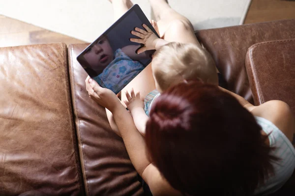 母親と赤ちゃんは自宅のソファでタブレットPCを再生して読み取ることを探しています — ストック写真
