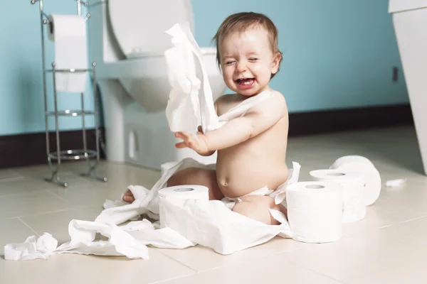Toddler ripping up toilet paper in bathroom Stock Photo