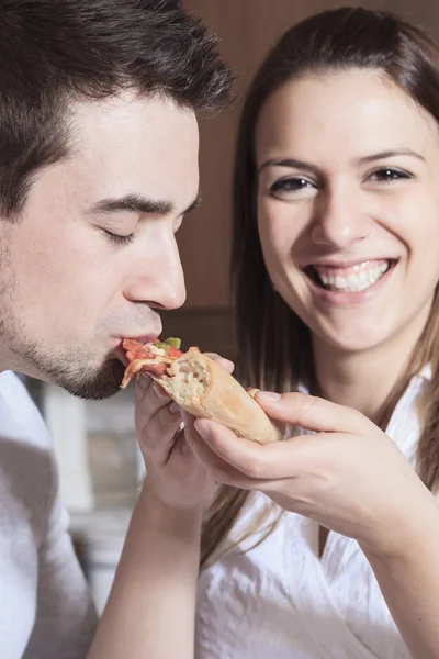 Happy young couple eating pizza at the kitchen — Stock Photo, Image