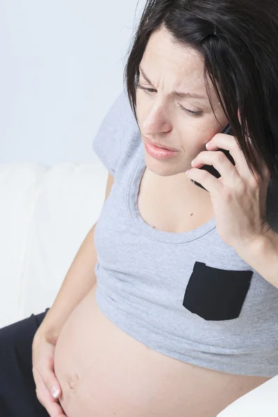 Pregnant woman sitting on the sofa with a telephone — Stock Photo, Image