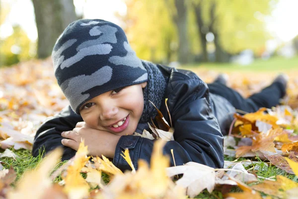 Roztomilý chlapec s podzimní listí v parku — Stock fotografie