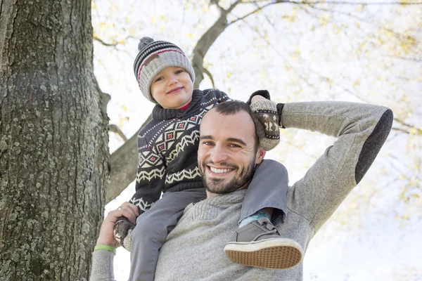 Retrato de pai feliz dando passeio de piggyback filho em seus ombros no parque de outono . — Fotografia de Stock