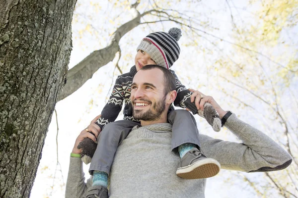 Retrato de pai feliz dando passeio de piggyback filho em seus ombros no parque de outono . — Fotografia de Stock