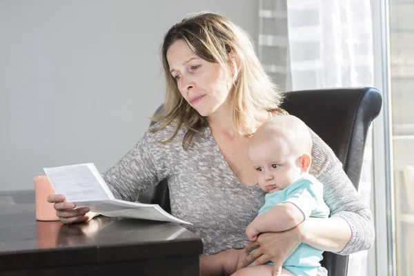 Mère tenant bébé et tapant sur ordinateur portable dans la cuisine . — Photo