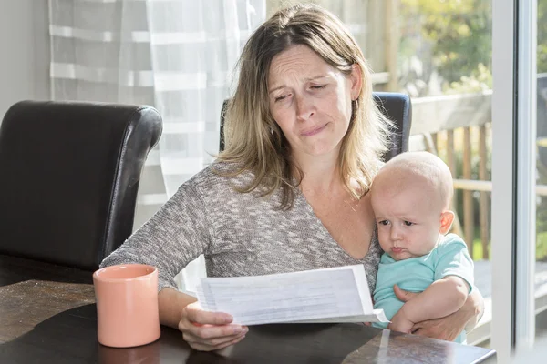 Mother holding baby  and typing on laptop computer in kitchen. — Stock Photo, Image