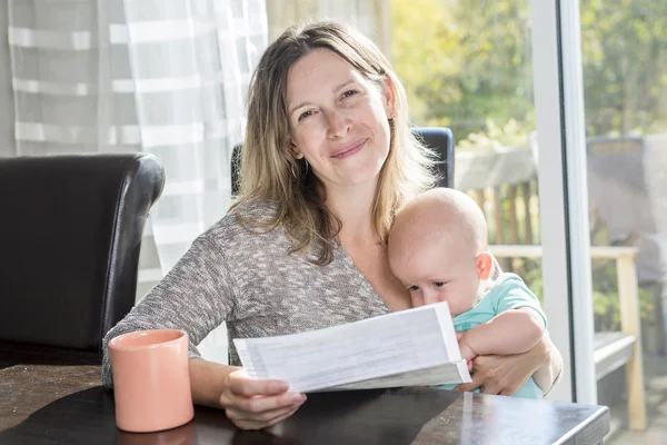 Mère tenant bébé et tapant sur ordinateur portable dans la cuisine . — Photo