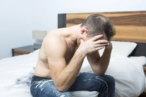 Chory człowiek siedzi na łóżku z głową na ręce — Zdjęcie stockowe
