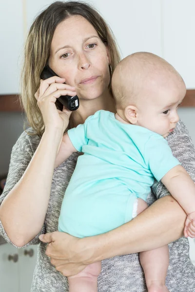 Woman on the phone while holding her baby in her arms in the kit — Stock Photo, Image