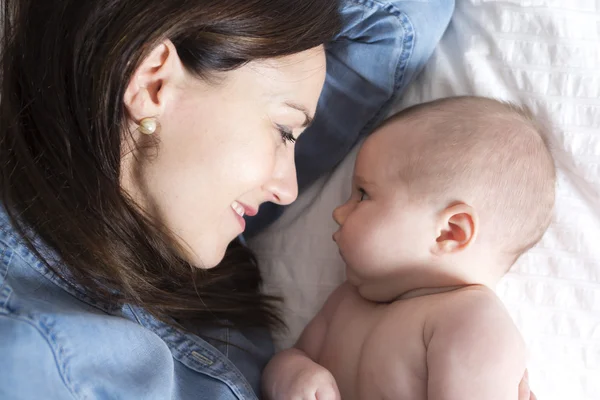 Bebê e mãe na cama branca tendo bom tempo — Fotografia de Stock