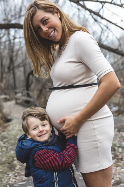 Gelukkig kind houden buik van zwangere vrouw in het bos — Stockfoto