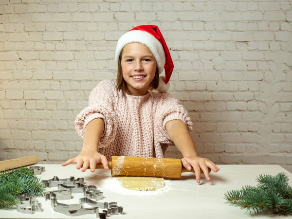 Щаслива дівчина в різдвяному капелюсі робить тісто для різдвяного печива на кухні, різдвяне печиво випічка — стокове фото