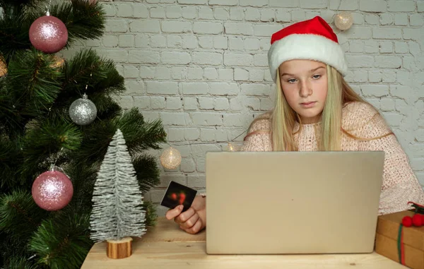 Happy girl w kapeluszu Santa trzymając karty kredytowe i zakupy online na prezenty świąteczne w domu — Zdjęcie stockowe