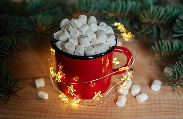 Hot chocolate cup with marshmallows with christmas lights and Christmas tree branches on the background — Stock Photo, Image