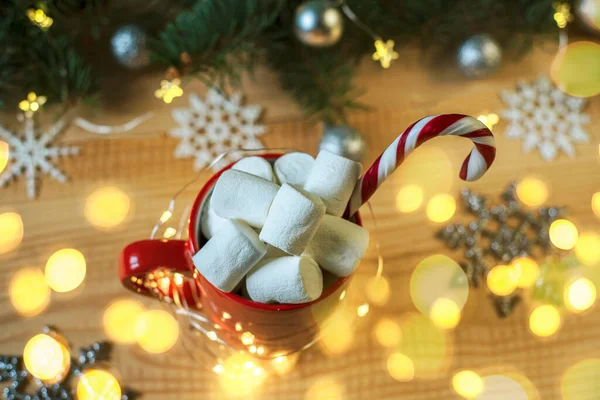 Christmas hot drink with marshmallows and candy cane with Christmas lights and ornaments on the background — Stock Photo, Image