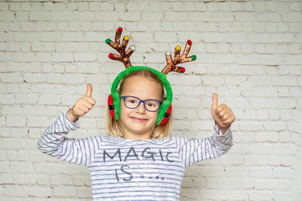 Щаслива дівчина в Різдвяних оленячих рогах і окулярах з її великими пальцями вгору, погана корекція зору — стокове фото