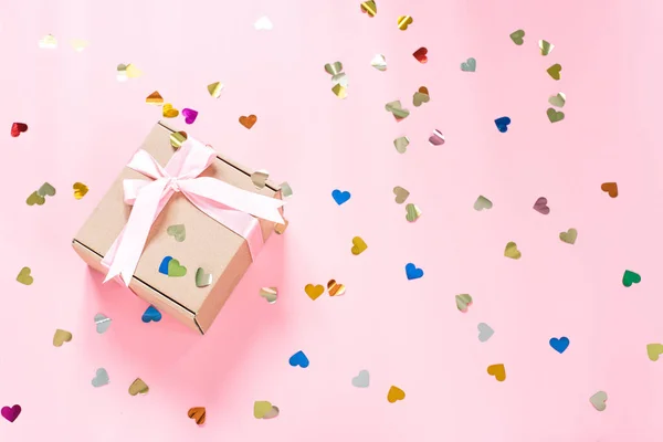 Caja de regalo con lazo de cinta rosa y confeti en forma de corazón sobre fondo rosa —  Fotos de Stock