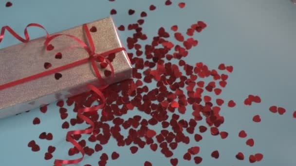 Конфетті у формі серця падає на подарункову коробку на синьому фоні — стокове відео