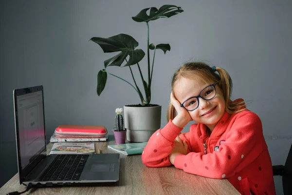 Glimlachend klein meisje in bril online studeren en met behulp van haar laptop thuis — Stockfoto